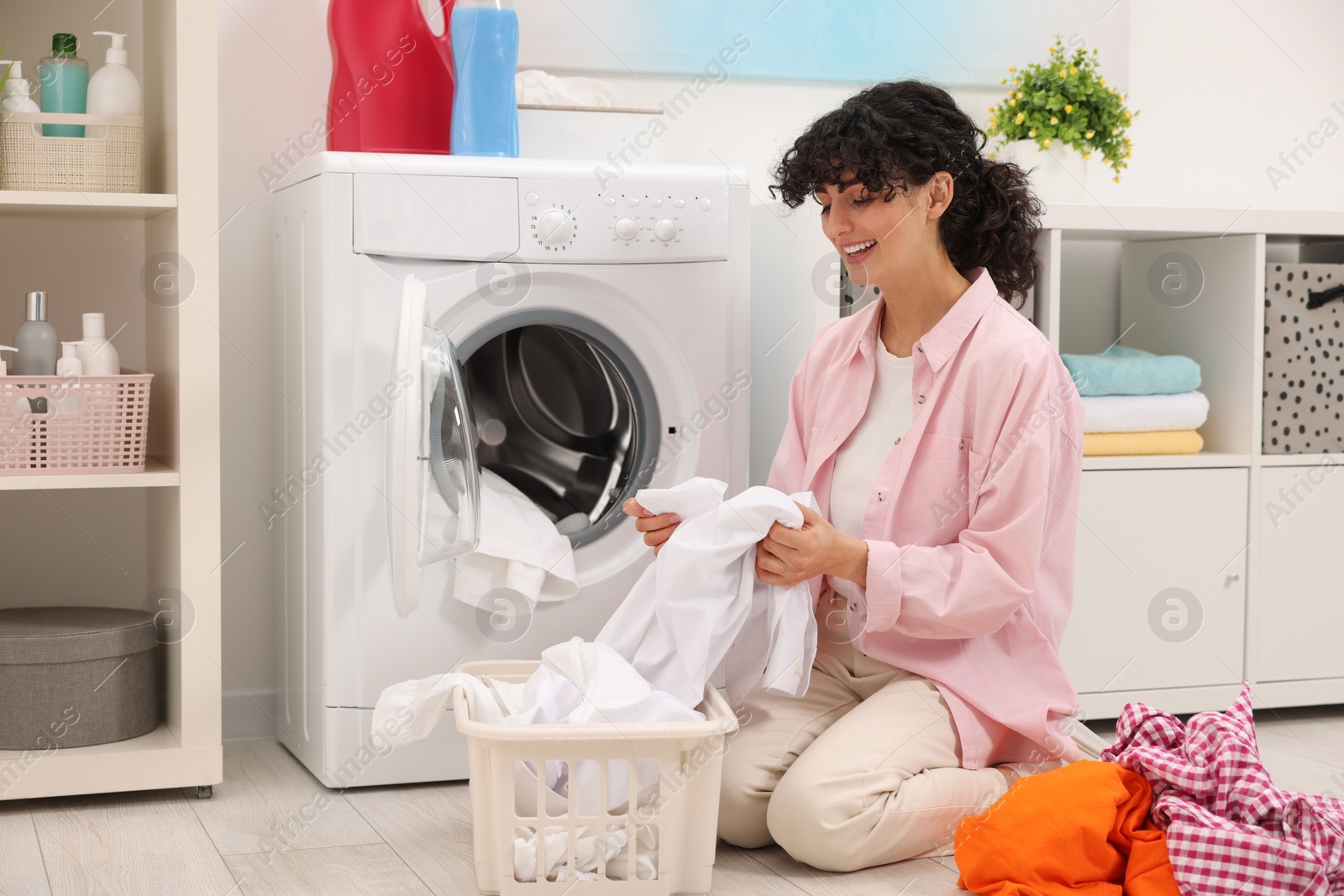 Photo of Happy woman with laundry near washing machine indoors