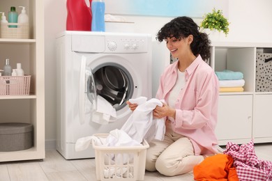 Photo of Happy woman with laundry near washing machine indoors