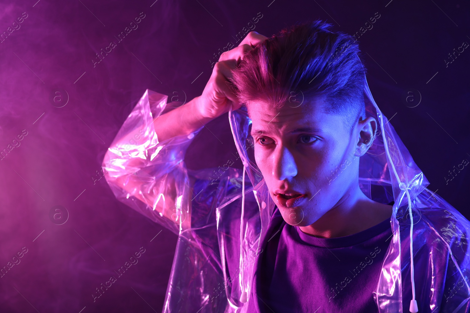 Photo of Young man wearing clear coat in neon lights with smoke effect. Space for text