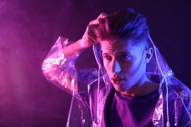 Photo of Young man wearing clear coat in neon lights with smoke effect. Space for text