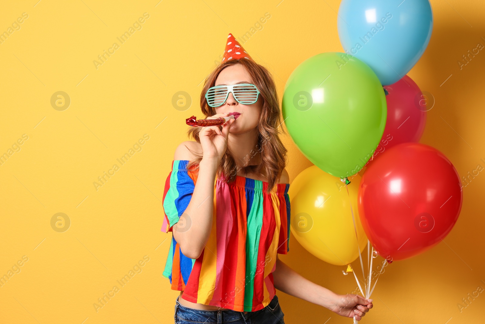 Photo of Young woman with bright balloons and party blower on color background. Birthday celebration