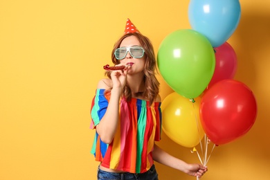 Photo of Young woman with bright balloons and party blower on color background. Birthday celebration