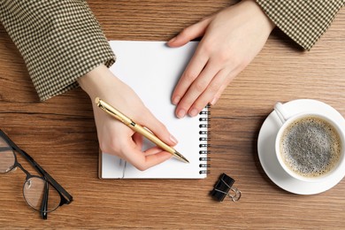 Photo of Woman writing in notebook at wooden table, top view