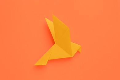 Beautiful origami bird on orange background, top view