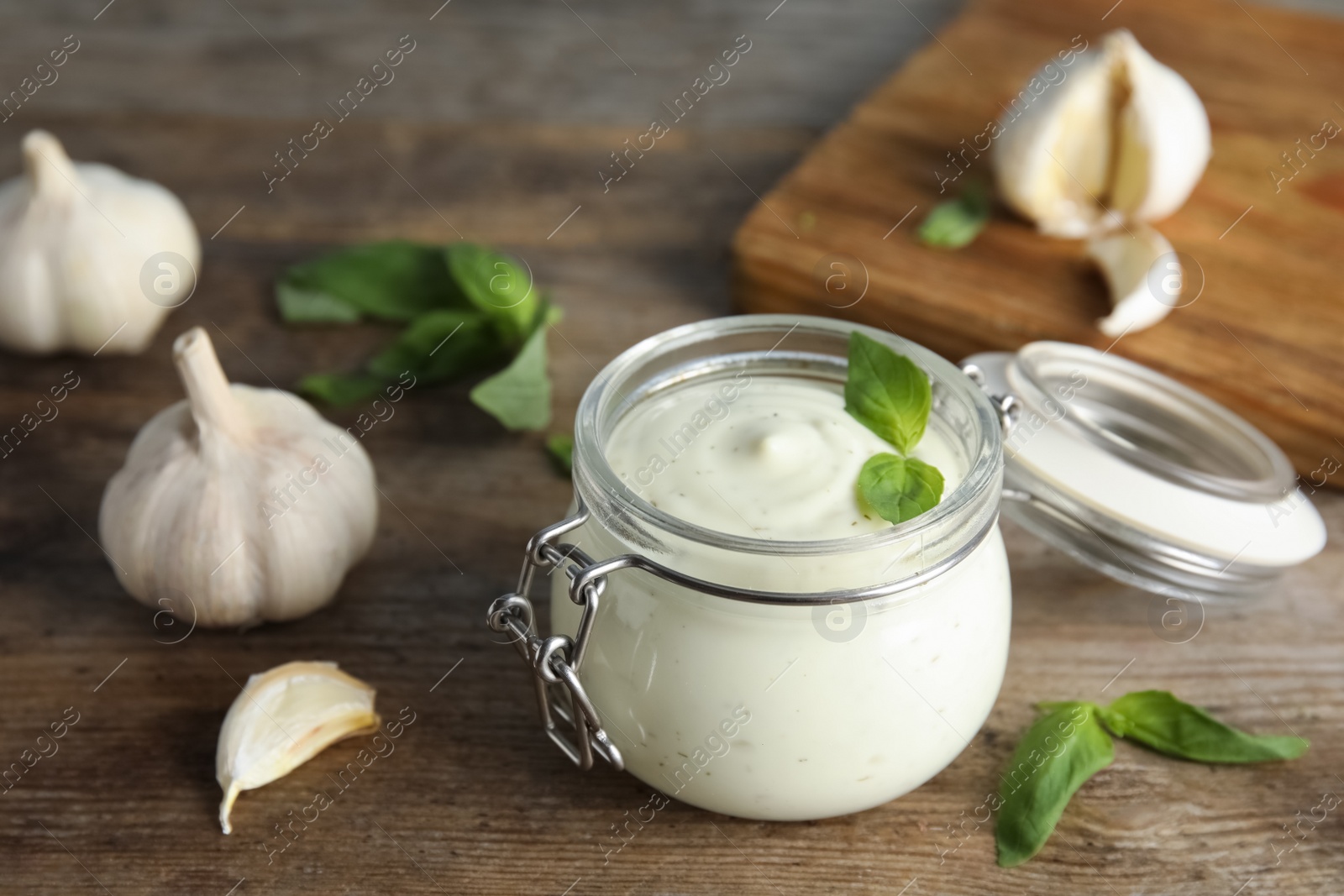 Photo of Composition with jar of garlic sauce on wooden table