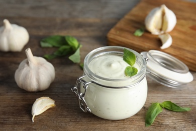 Photo of Composition with jar of garlic sauce on wooden table