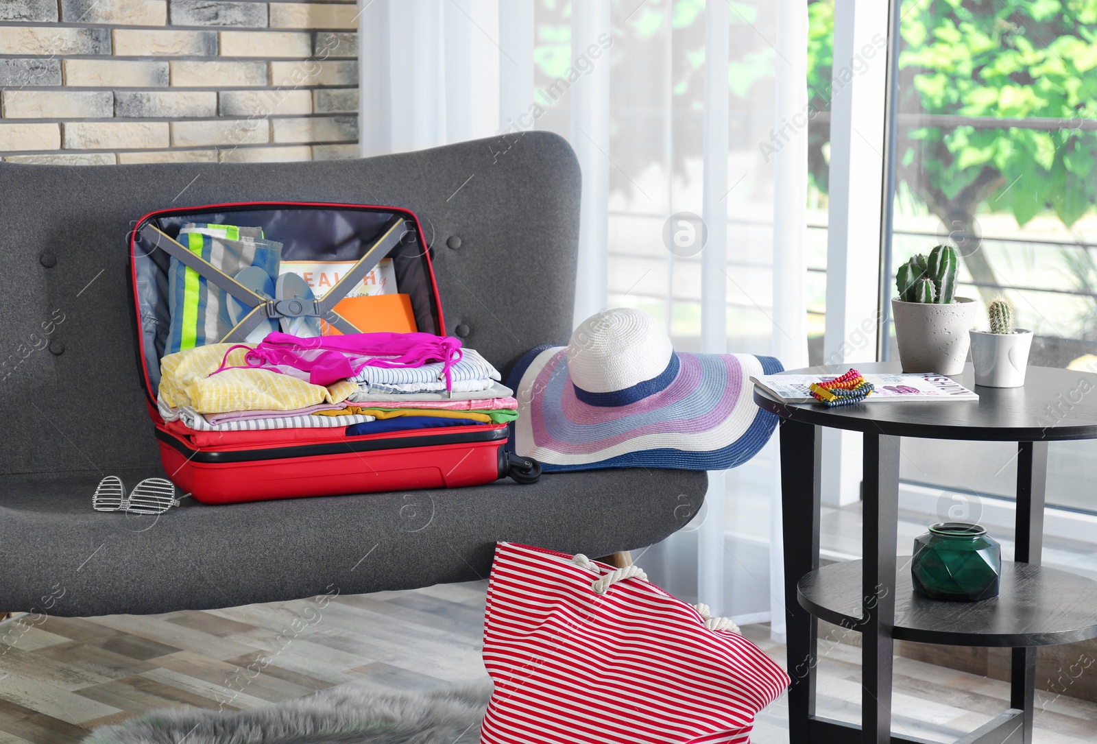 Photo of Open suitcase with different clothes and accessories on sofa indoors. Packing for vacation