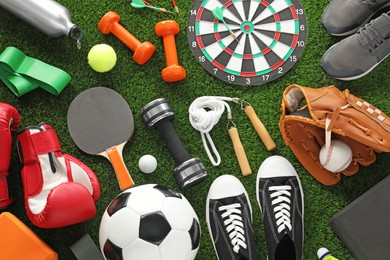 Photo of Different sport equipment and sneakers on green grass, flat lay