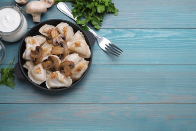 Delicious dumplings (varenyky) with potatoes, onion and mushrooms served on light blue wooden table, flat lay. Space for text