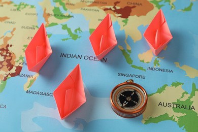 Bright paper boats and compass on world map, above view