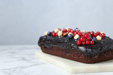 Photo of Delicious chocolate sponge cake with berries and nuts on white marble table, closeup. Space for text