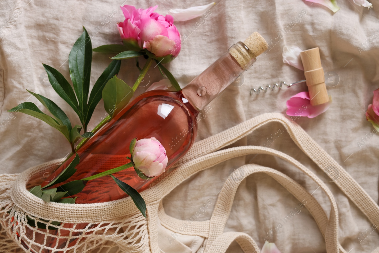 Photo of Flat lay composition with rose wine, mesh bag and beautiful peonies on white fabric