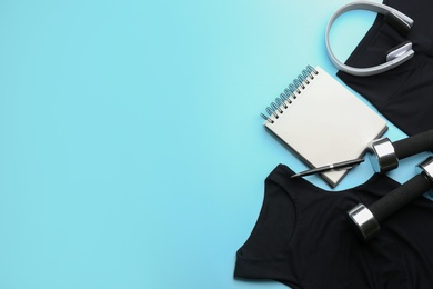 Flat lay composition with sportswear, notebook and dumbbells on light blue background, space for text. Gym workout plan