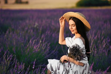 Photo of Beautiful young woman with bouquet sitting in lavender field