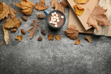 Flat lay composition with cup of hot drink and autumn leaves on grey table, space for text. Cozy atmosphere