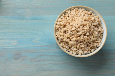 Photo of Delicious pearl barley in bowl on light blue wooden table, top view. Space for text