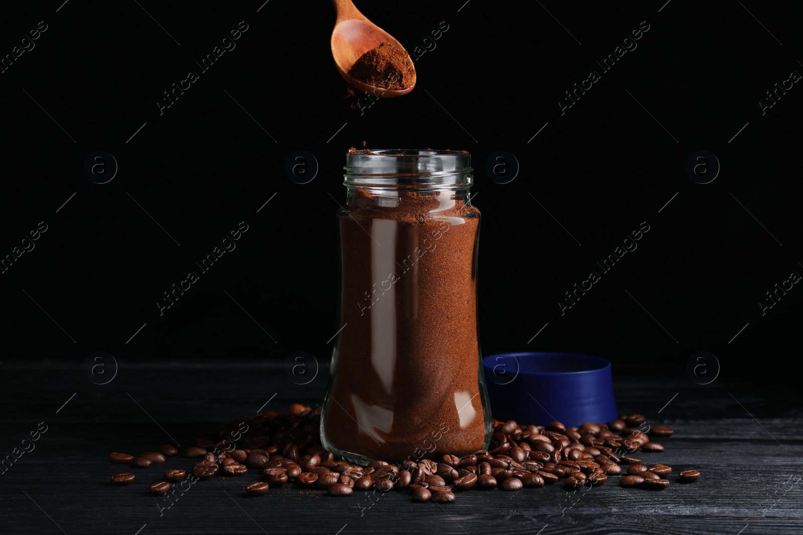 Photo of Putting ground coffee into glass jar on black wooden table