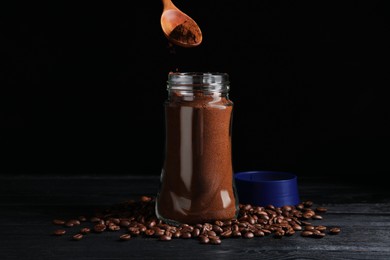 Photo of Putting ground coffee into glass jar on black wooden table