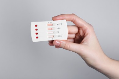 Photo of Woman holding disposable multi-infection express test on light grey background, closeup