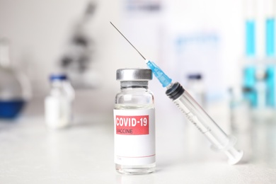 Photo of Vial with vaccine against Covid-19 and syringe on white table indoors