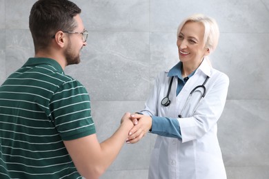 Photo of Doctor shaking hands with patient after consultation near grey wall