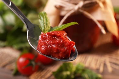 Holding spoon of tasty tomato paste and basil over table, closeup