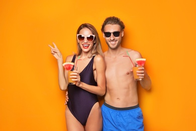 Happy young couple in beachwear with cocktails on color background