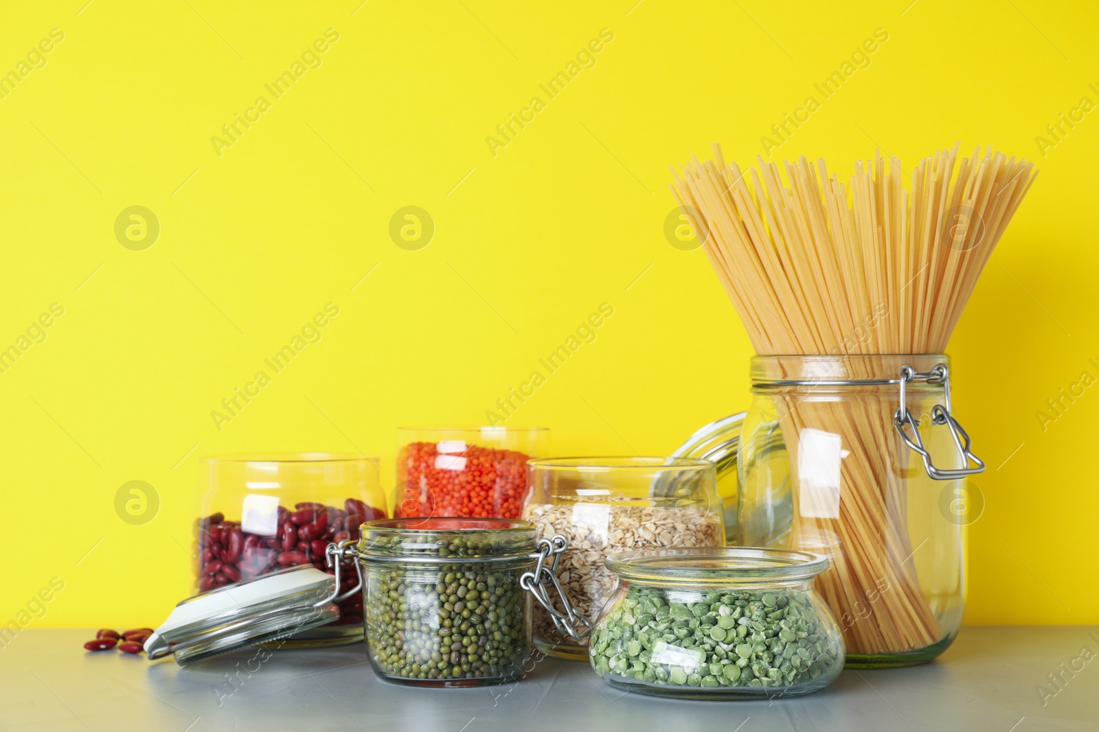 Photo of Glass jars with different types of groats and pasta on light grey table