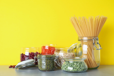 Glass jars with different types of groats and pasta on light grey table