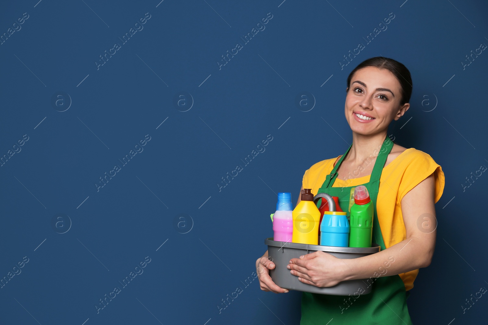 Photo of Woman with basin of detergents on color background. Space for text