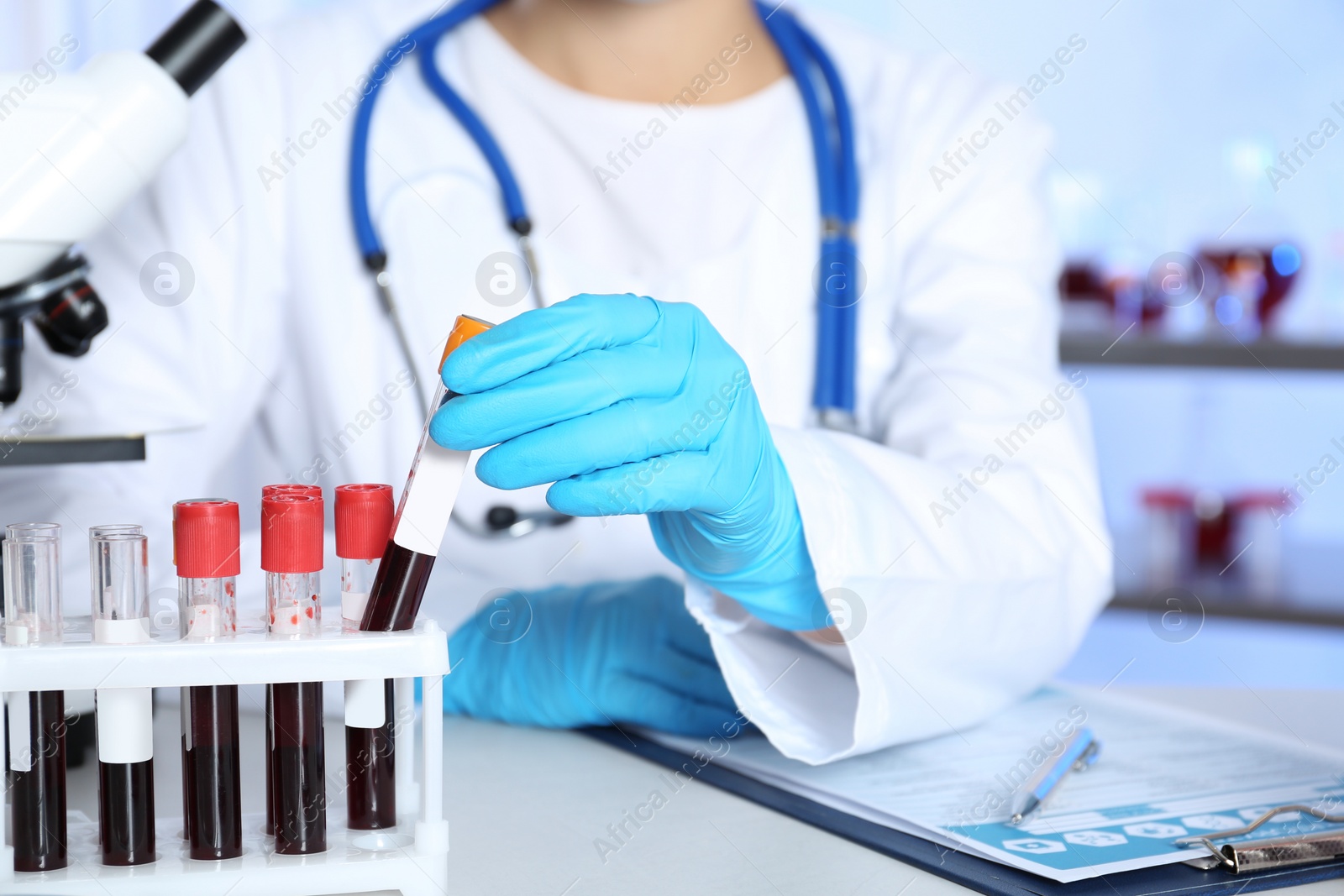 Photo of Laboratory worker taking test tube with blood sample from rack for analysis on table