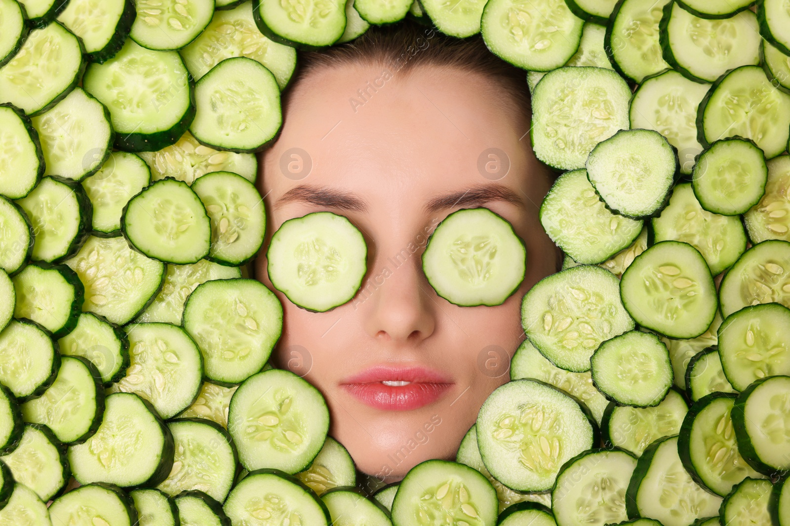 Photo of Beautiful woman among cucumber slices, top view