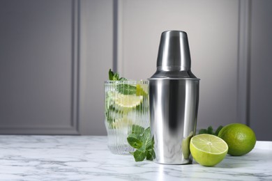 Photo of Metal cocktail shaker, delicious mojito, limes and mint on white marble table, space for text