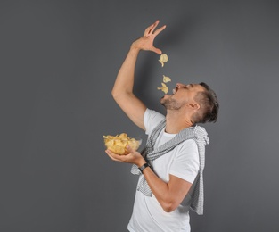 Photo of Man eating potato chips on grey background. Space for text