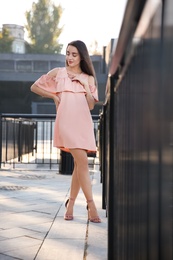 Photo of Beautiful young woman in stylish pink dress near railing outdoors