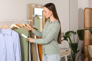 Young woman cleaning clothes with adhesive lint roller indoors