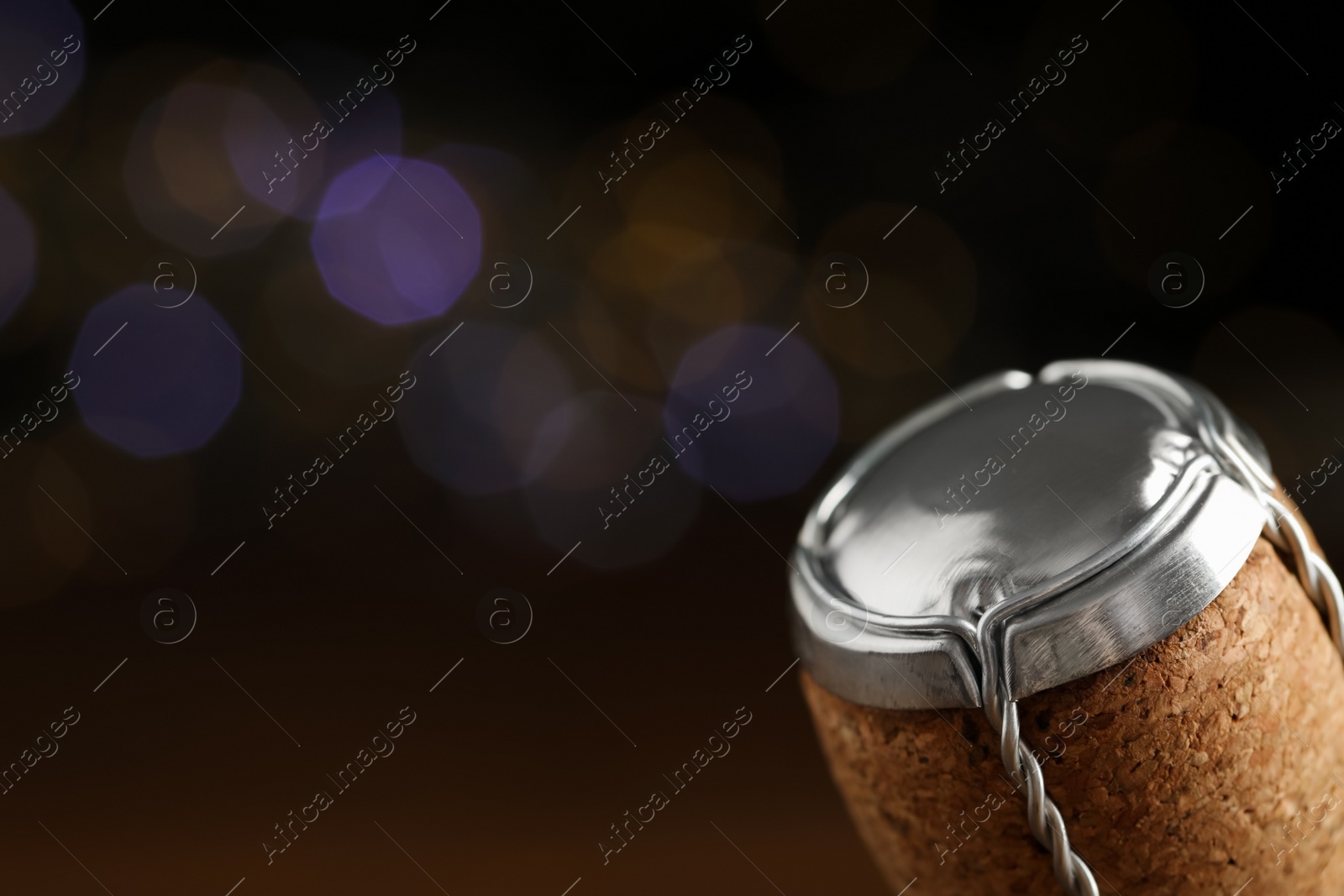 Photo of Sparkling wine cork with muselet cap against blurred festive lights, closeup. Space for text