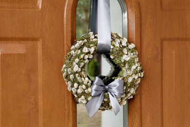 Photo of Wreath made of beautiful willow branches and grey bow on wooden door