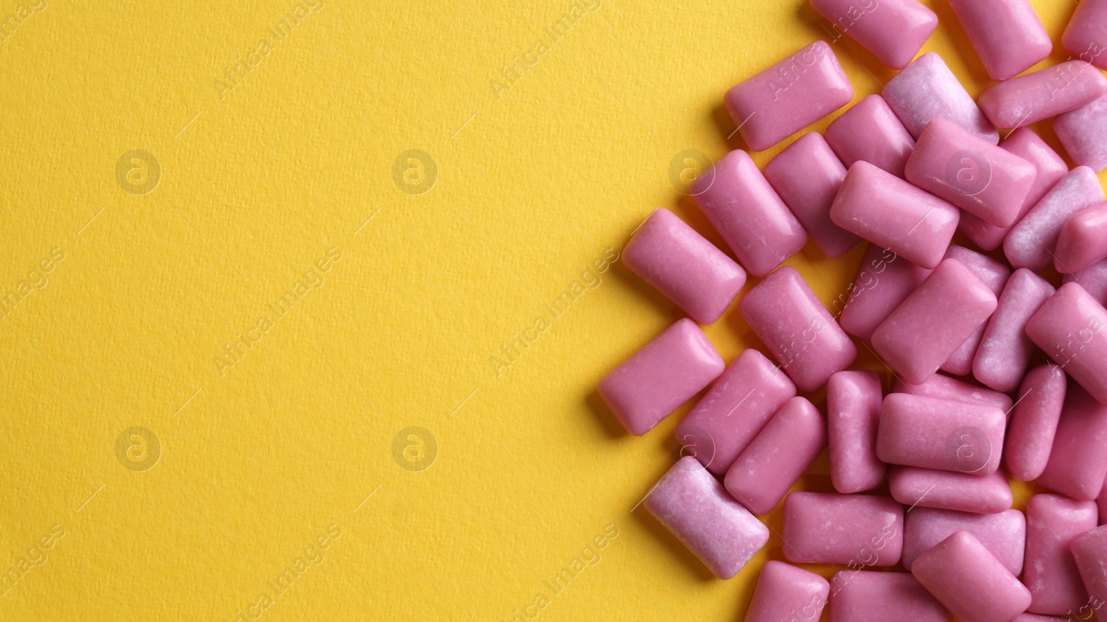 Photo of Sweet chewing gums on yellow background, flat lay. Space for text