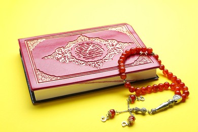 Photo of Muslim prayer beads and Quran on yellow background