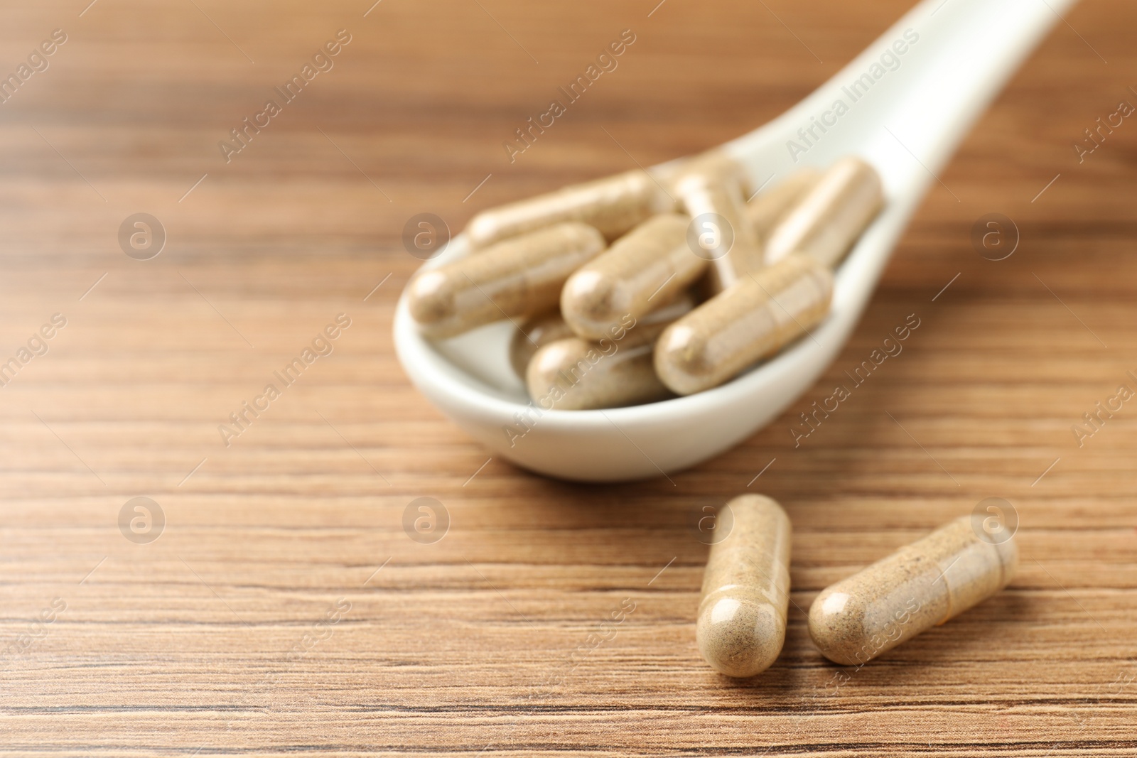 Photo of Dietary supplement capsules with spoon on wooden table, closeup. Space for text