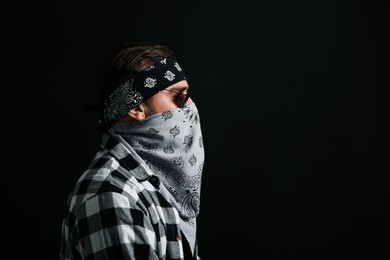 Photo of Fashionable young man with bandana covering his face on black background, space for text