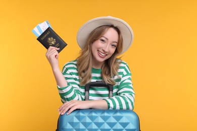 Happy young woman with passport, ticket and suitcase on yellow background