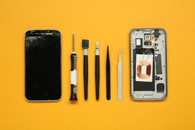 Damaged smartphone and repair tool set on orange background, flat lay