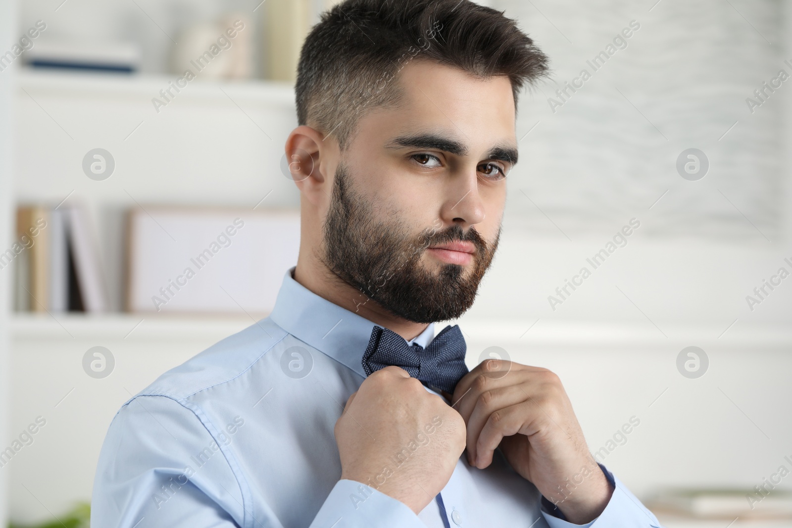 Photo of Portrait of handsome man adjusting bow tie indoors