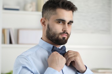 Photo of Portrait of handsome man adjusting bow tie indoors