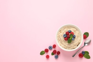 Tasty oatmeal porridge with raspberries and blueberries in bowl on pink background, flat lay. Space for text