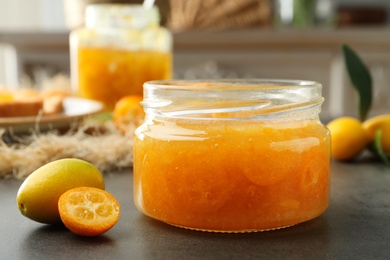 Photo of Delicious kumquat jam and fresh fruits on grey table, closeup