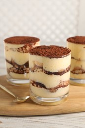 Photo of Delicious tiramisu in glasses and spoon on light wooden table