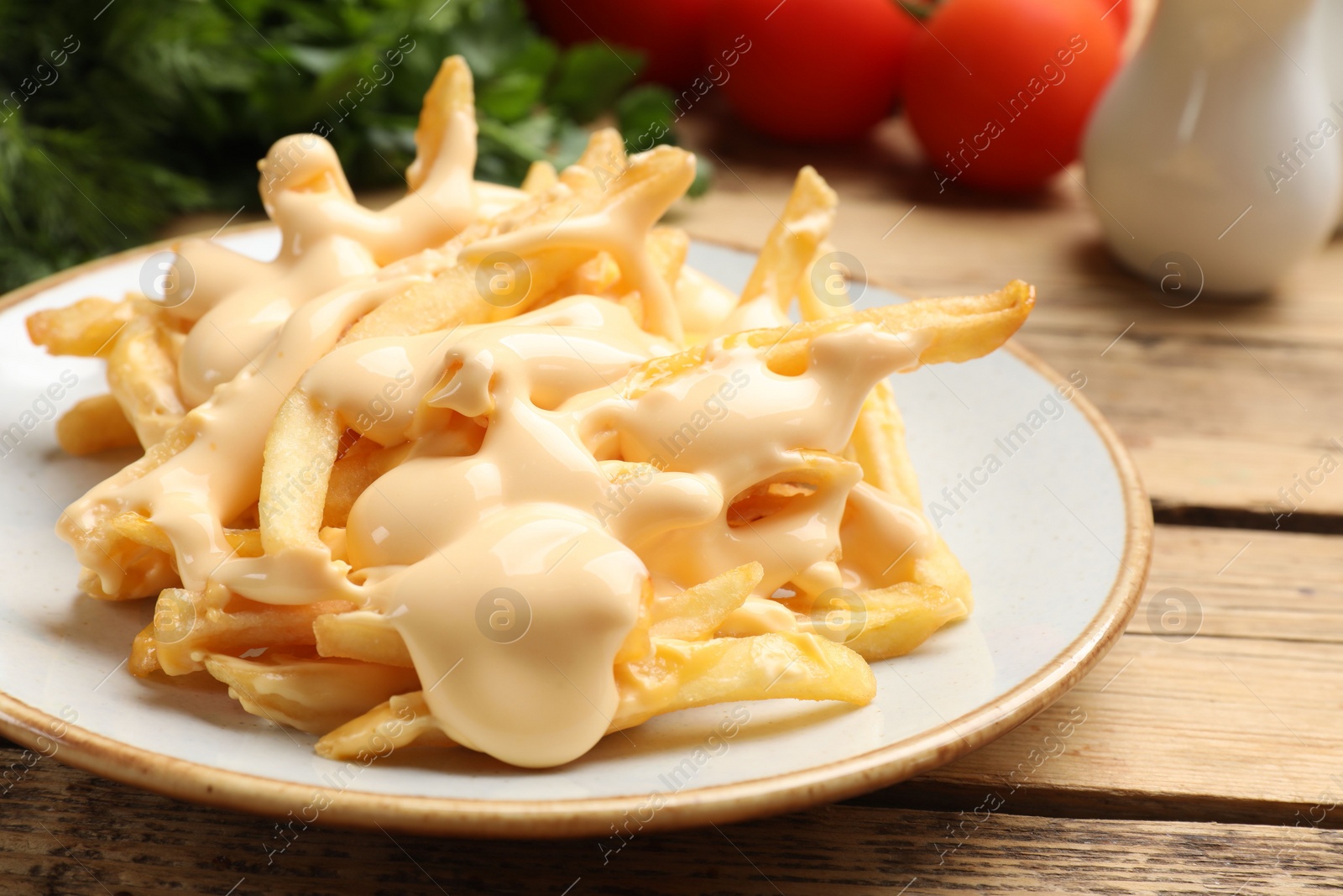 Photo of Delicious French fries with cheese sauce on wooden table, closeup